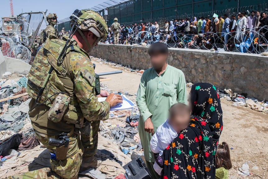 An Australian solider checks the paperwork of a young family. 