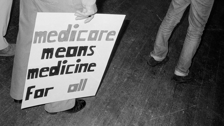A black and white photo of a sign reading 'Medicare means medicine for all'