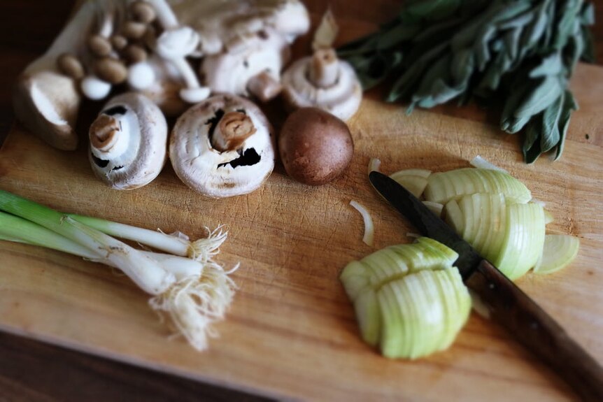 Mushrooms and spring onions lie on a wooden chopping board.