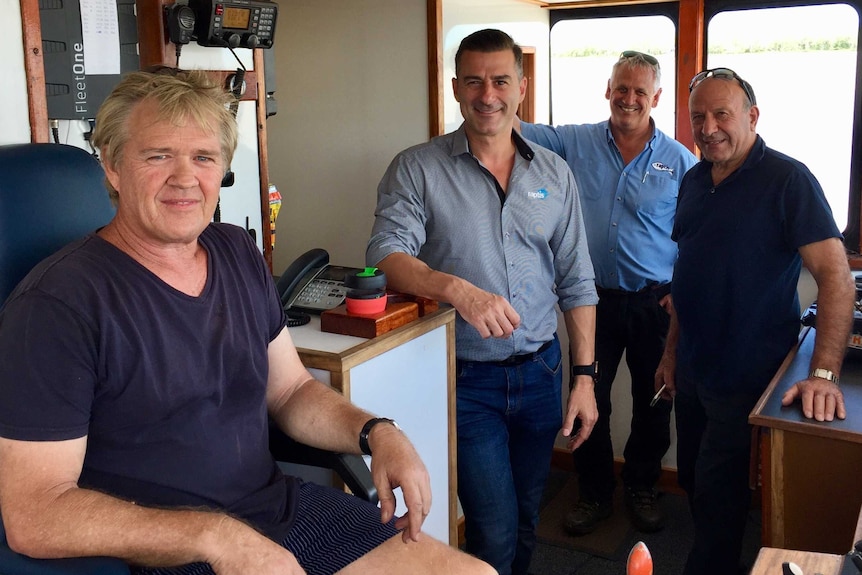 Four fishermen stand in the wheelhouse of a refurbished trawler.