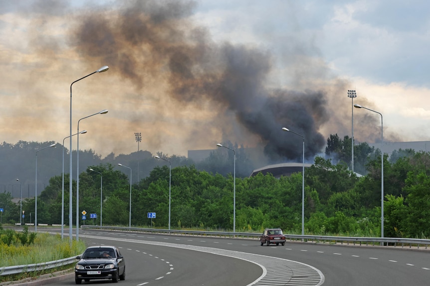 Black smoke rises in the distance behind a deserted highway.