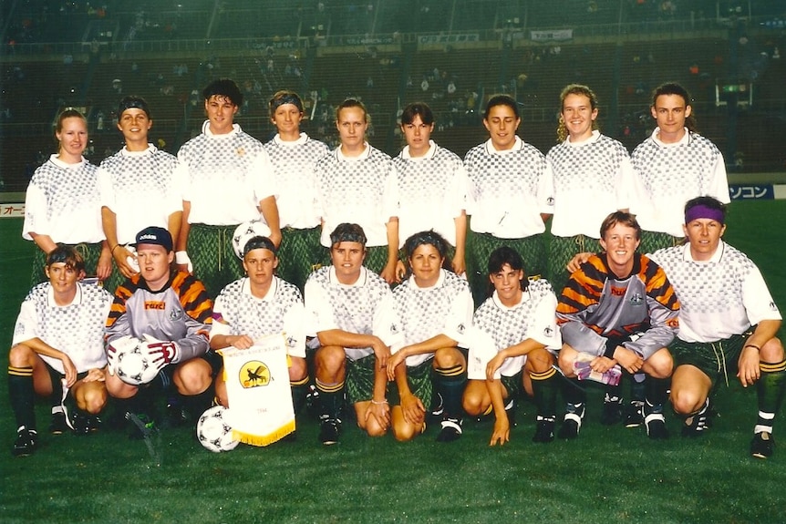 A soccer team wearing white and green poses for a photo before a game