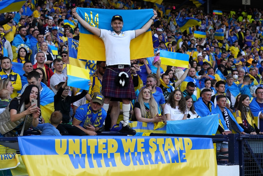A man in a kilt holds a Ukraine flag above his head
