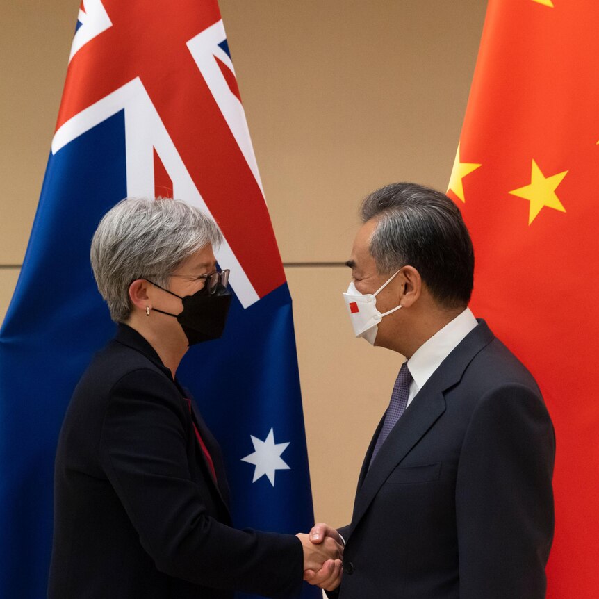 A man and a woman wear face masks as they shake hands in front of the flags of Australia and China.