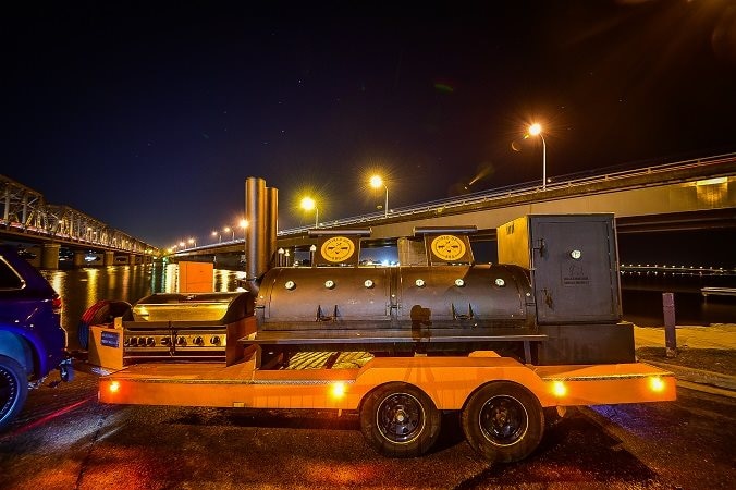 A large barbecue and smoker on a trailer towed by a car at night.