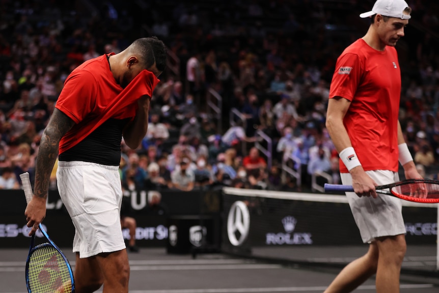 Nick Kyrgios holds his shirt over his face as John Isner looks downwards beside him