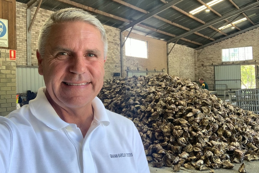 Man stands in front of huge pile of shucked oyster shells. 