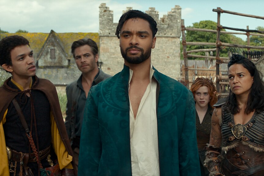Two men of colour, one woman of colour, one white man and one white girl stand in a stone village wearing medieval attire.