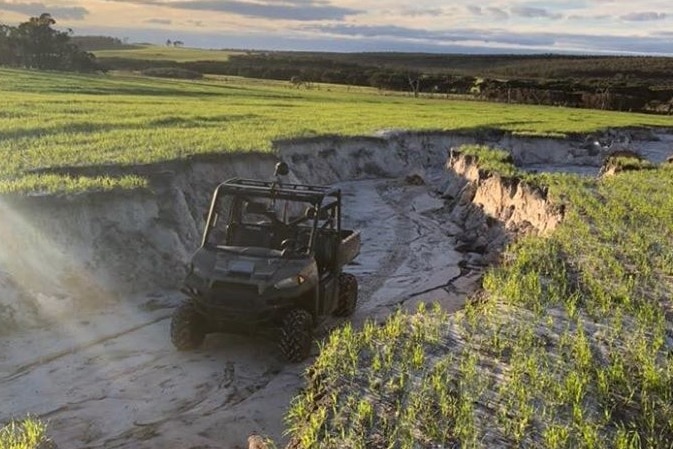 A car sits in a deep ditch.