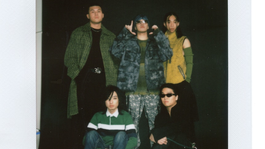 Polaroid of five men in streetwear, three are standing and two are sitting at their feet.
