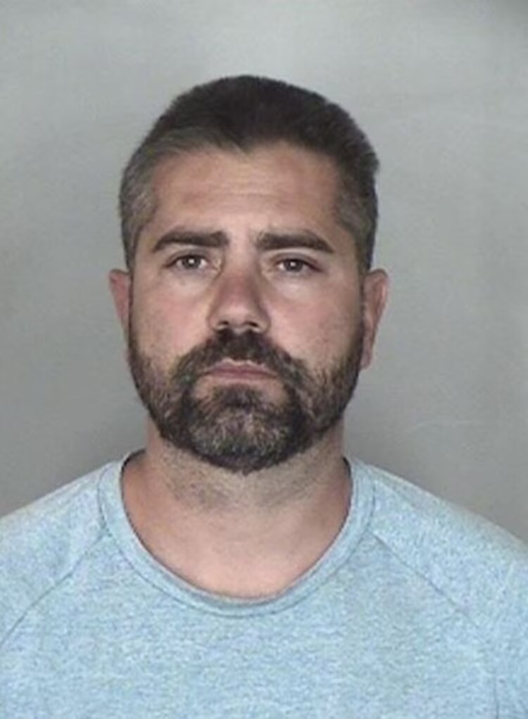 A mugshot of a bearded man in a grey t shirt 