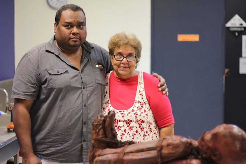 An Aboriginal man and woman embrace with the mummified remains of their ancestor in front of them.