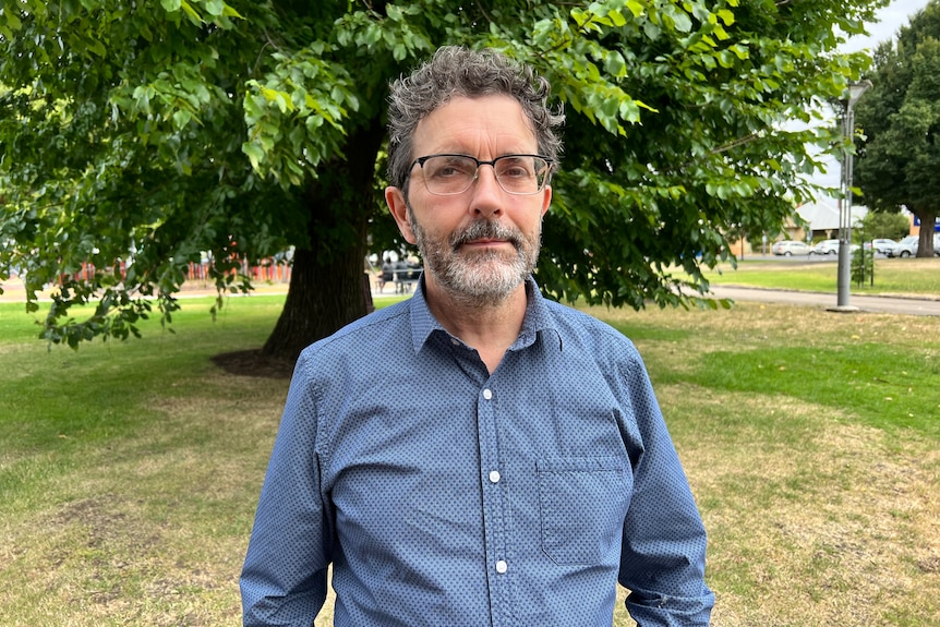 A man with grey hair, a beard and glasses looks at the camera.