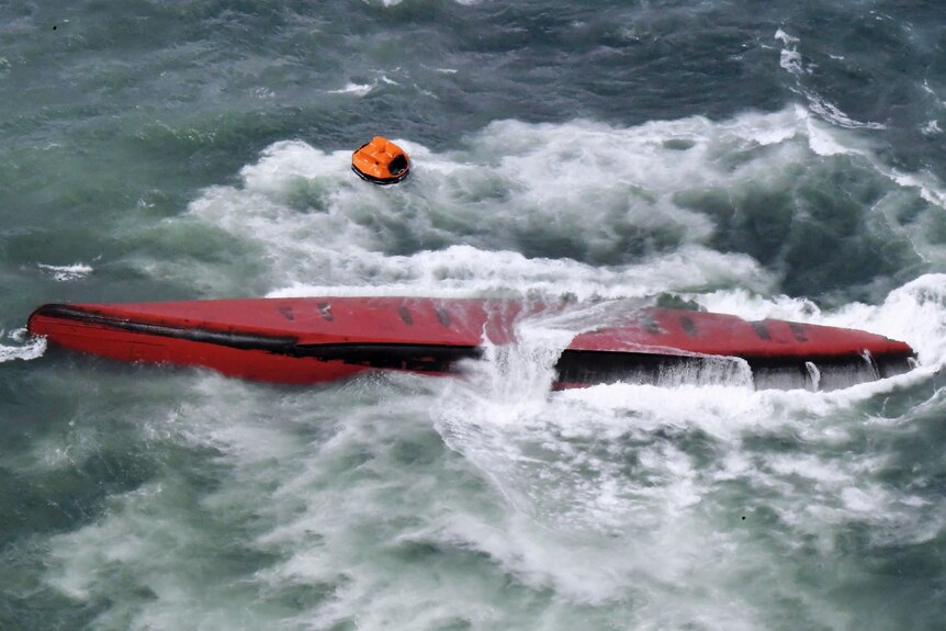 A shipping tanker sits upside down in rough seas with only its red underside visible