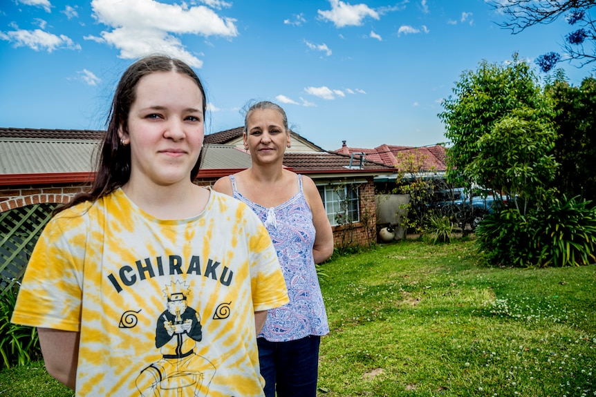 A middle aged woman out the front of a house with her daughter in the foreground