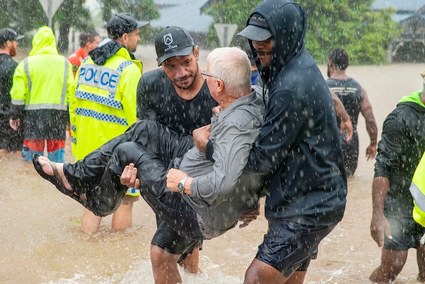 Two young men carry an elderly man through flood waters