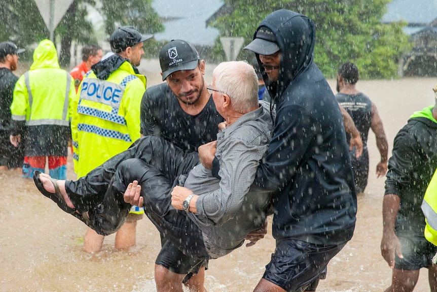 Five Fijian men stand around small boat on floodwater. 