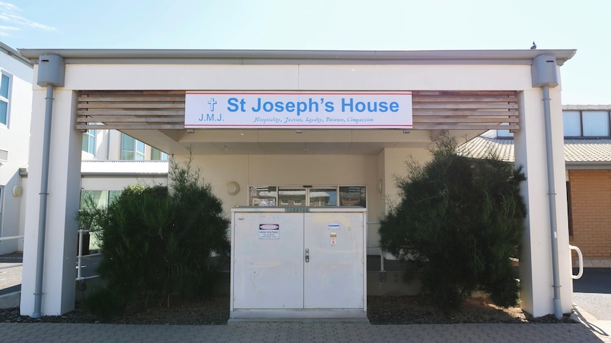 A front view of a building with a verandah over hedges and an electricity box of St Joseph's House.