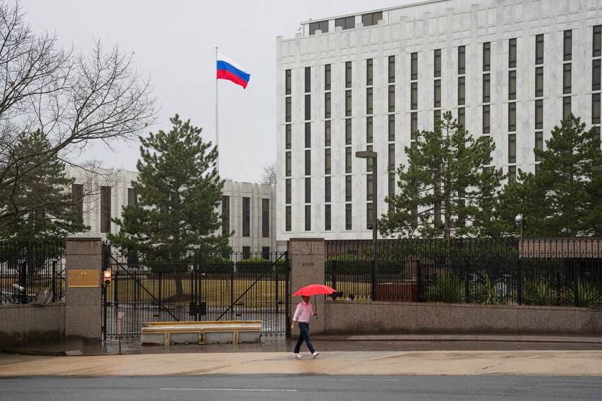 Un peatón camina con un paraguas frente a la Embajada de Estados Unidos en la Federación Rusa.