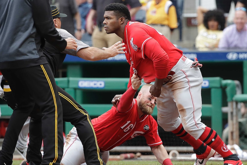 A baseball player evades an ankle tap from his own player as he looks to join a fight on a baseball pitch