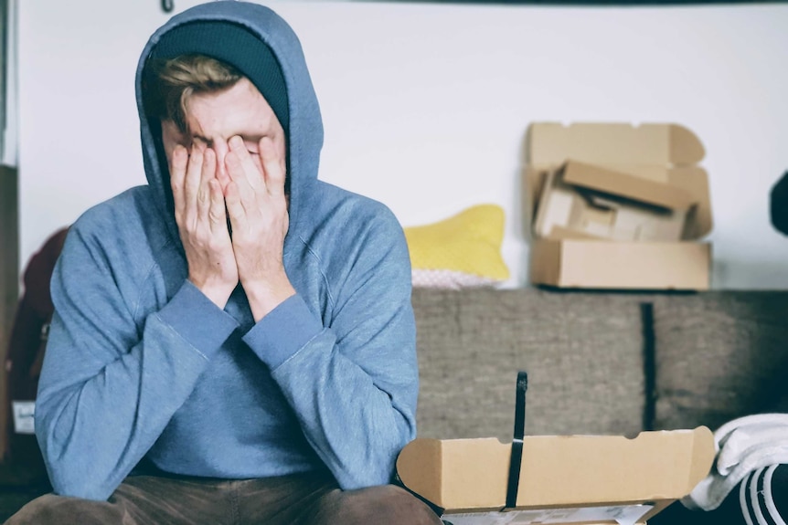 Man in blue hoodie sits down with head in his hands