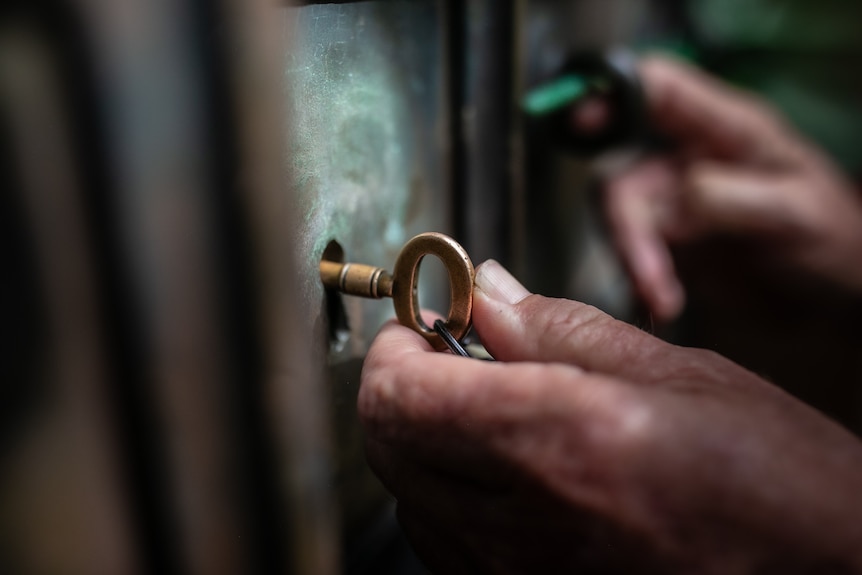 A hand turns a brass key in a lock.