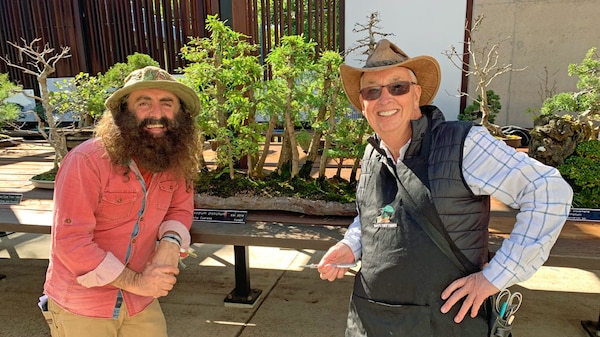 Costa with horticultarist standing in front of a table with a bonsai tree.