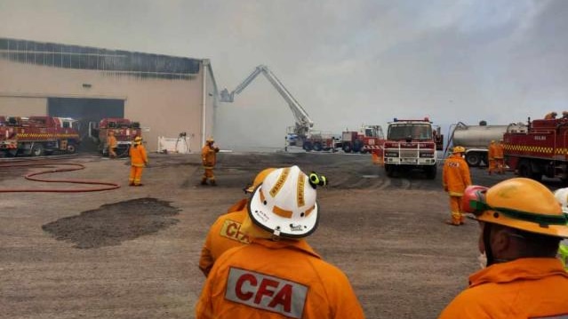 Smoke fills the air around a damaged hay shed as fire fighters look on. 