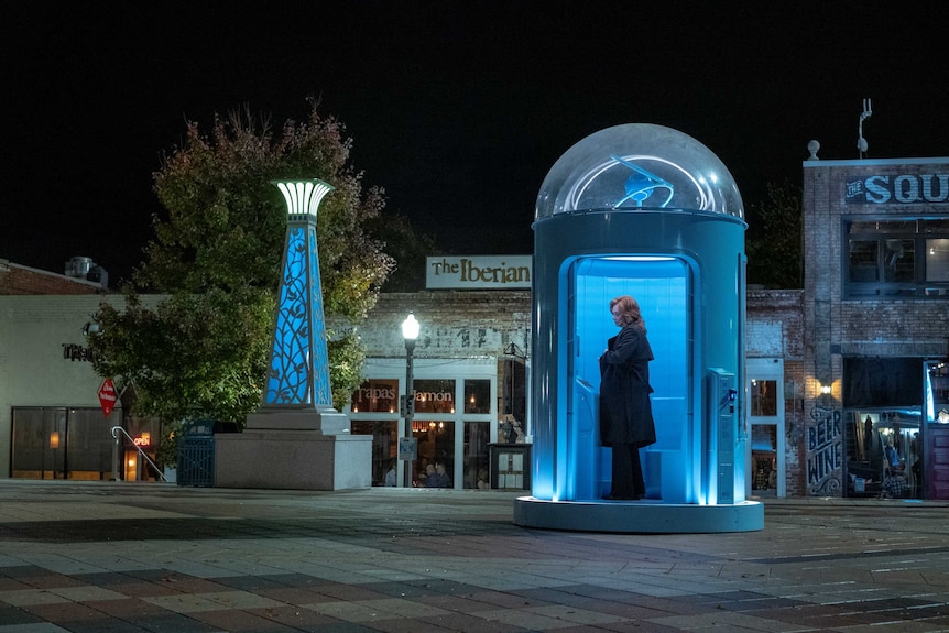 Jean Smart playing Agent Blake standing in a big blue phone booth in the show Watchmen
