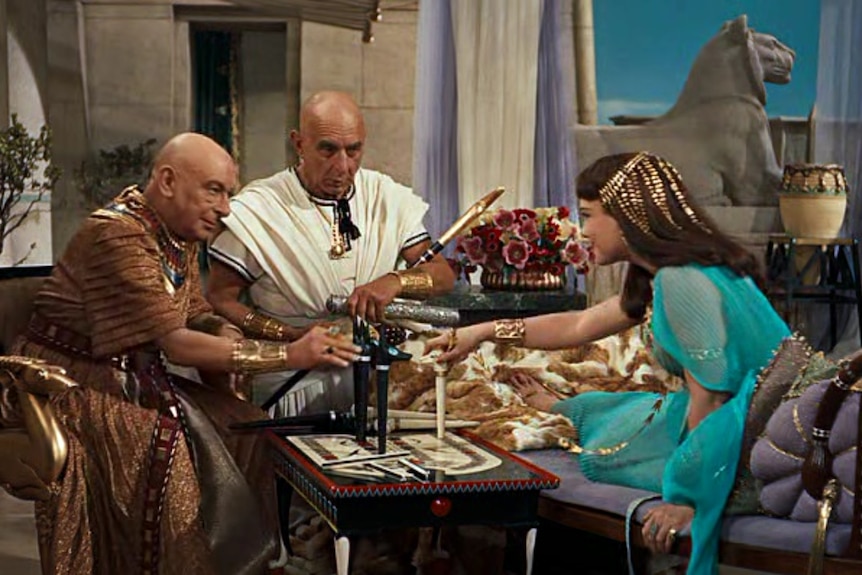 Two men and a woman dressed in elaborate costumes sitting around an ancient-style of board game in the film The 10 Commandments