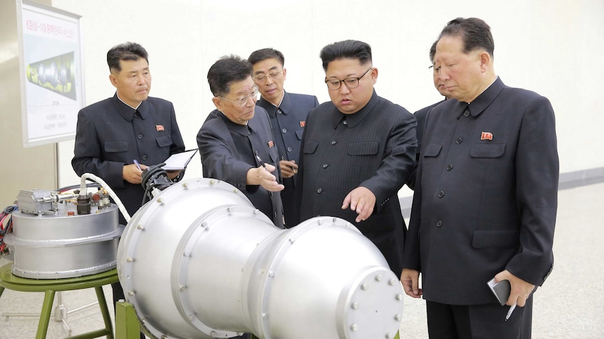 Kim Jong-un, flanked by men, points at a warhead.