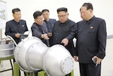 Kim Jong-un, flanked by men, points at a warhead.