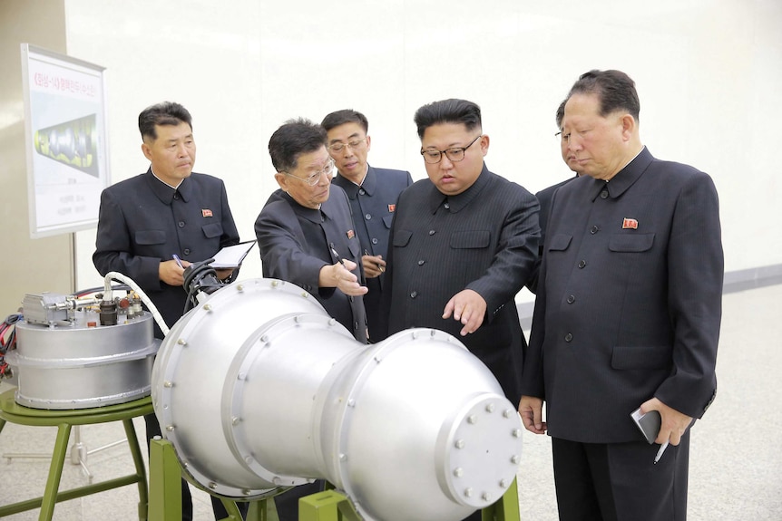 Kim Jong-un, flanked by men, points at a warhead.