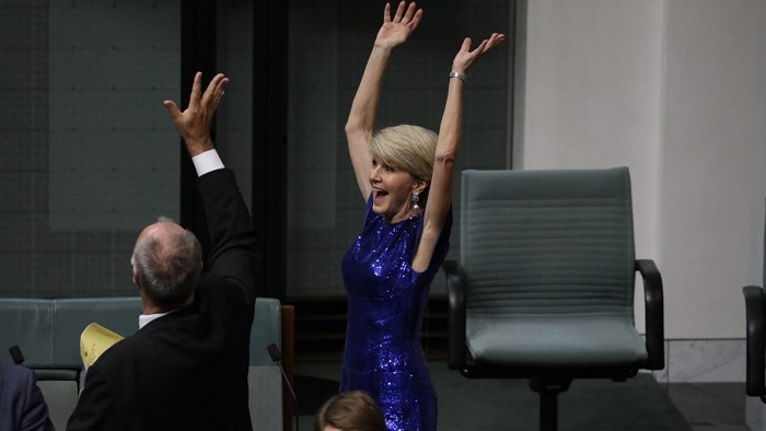 A picture of Julie Bishop wearing a blue sparkling dress with her hands in the air and a surprised expression.