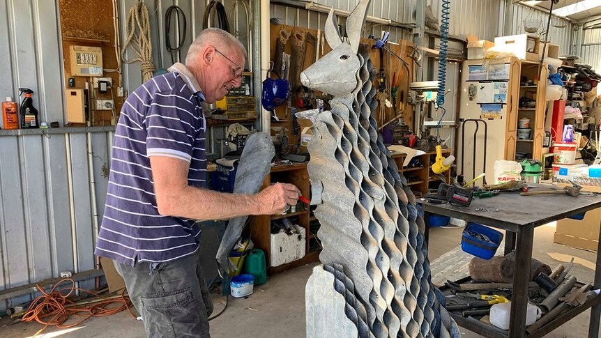 A man is drawing on a metal sculpture of a kangaroo he is making.