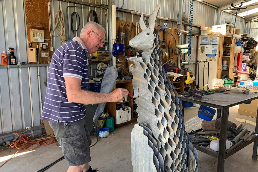 A man is drawing on a metal sculpture of a kangaroo he is making.