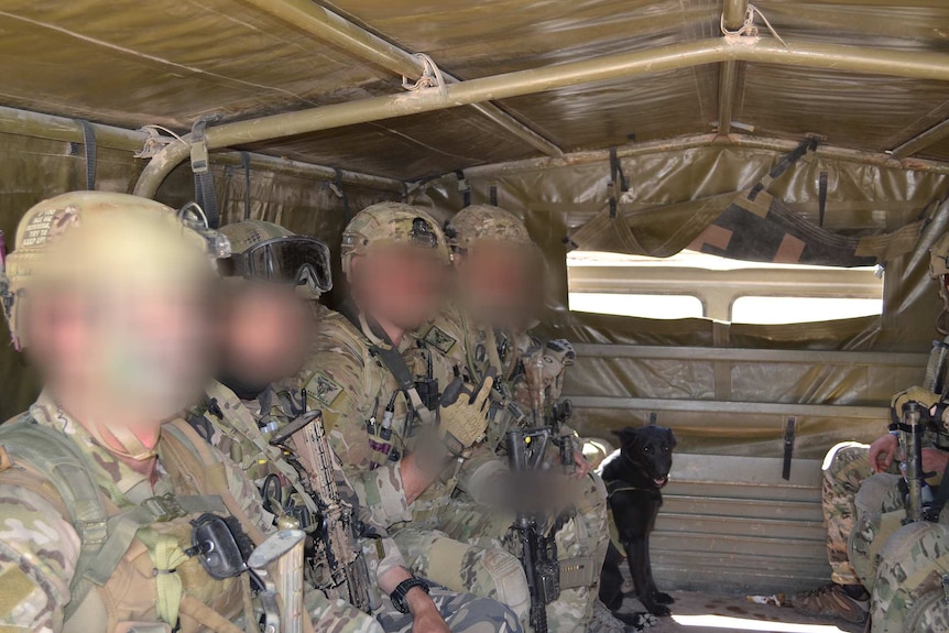 About six men in uniforms sitting in the back of a vehicle with faces blurred.