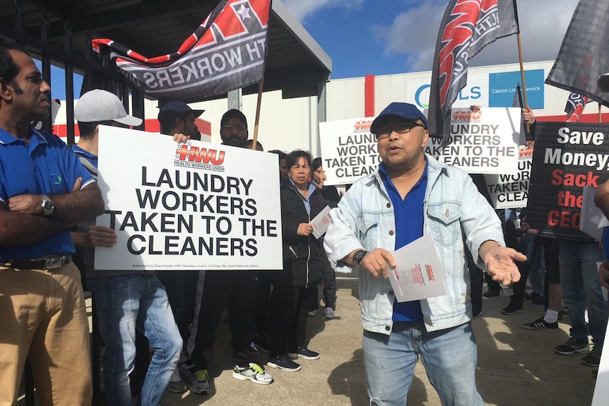 Workers rall outside Cabrini Linen Services, holding signs that say ' Laundry workers taken to the cleaners'.
