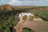 an aerial shot of a hostel nestled in the bush between red rock landscape