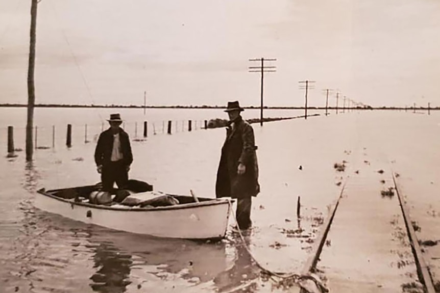 Historic photo of two men in boat in floodwaters in 1950s along rail line near Winton in western Queensland.