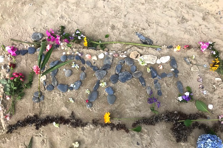 Pebbles arranged to spell Toyah and surrounded by flowers on Wangetti Beach