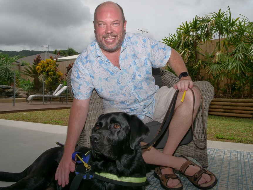 Dale Reardon and his black labrador assistant dog Cookie on the deck of his Cairns home. 