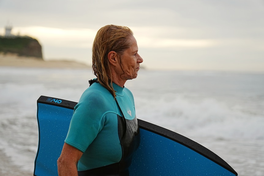 Elderly woman in blue wetsuit holding boogie board.
