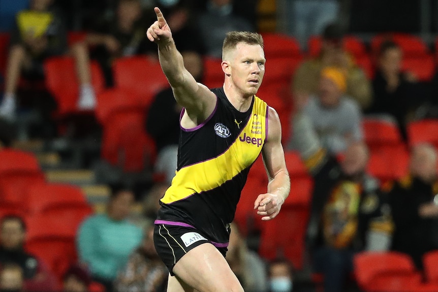 A Richmond AFL player points a finger on his right hand as he celebrates kicking a goal.