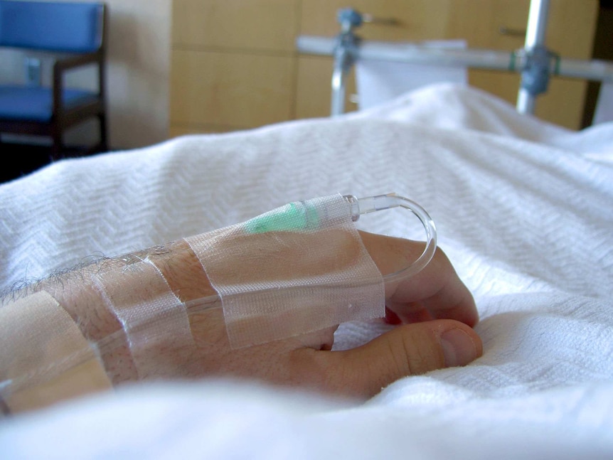A man's hand rests on a hospital bed.