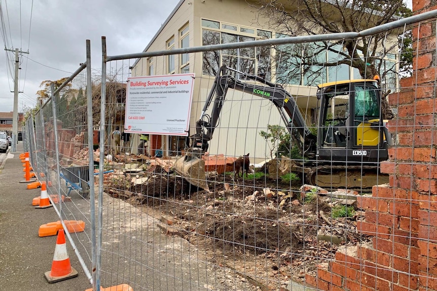 A partly demolished red brick fence, at a construction site.