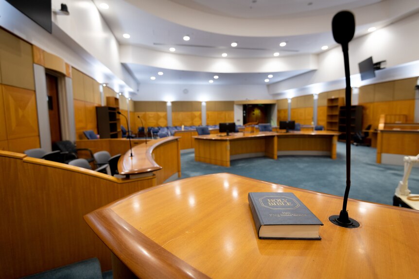 The witness stand inside the Supreme Court of the NT. There's a Bible in the foreground and a microphone.