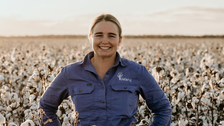 A young woman wearing a work shirt stands in a field of cotton
