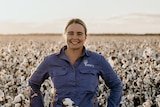 A young woman wearing a work shirt stands in a field of cotton