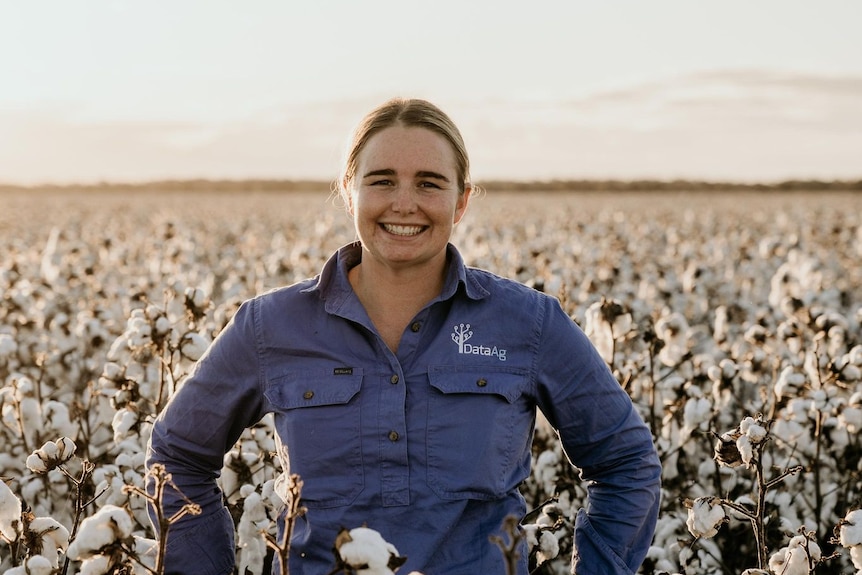 A lady wearing a work shirt standing in a field of cotton